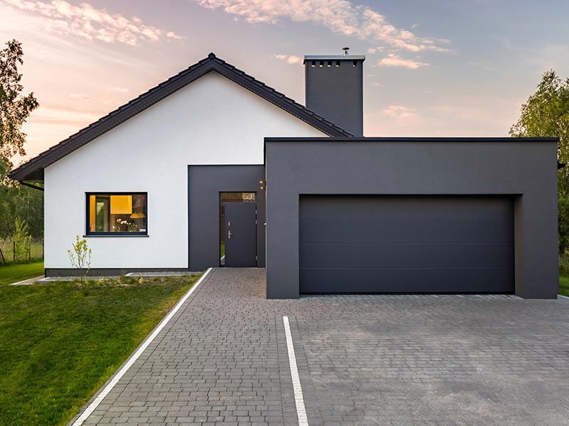 Concept image with a wide grey garage door and a white house in the background.