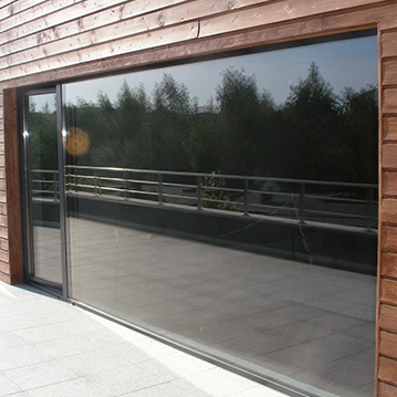 A wide glass window reflecting forest and concrete in beautiful sunlight.